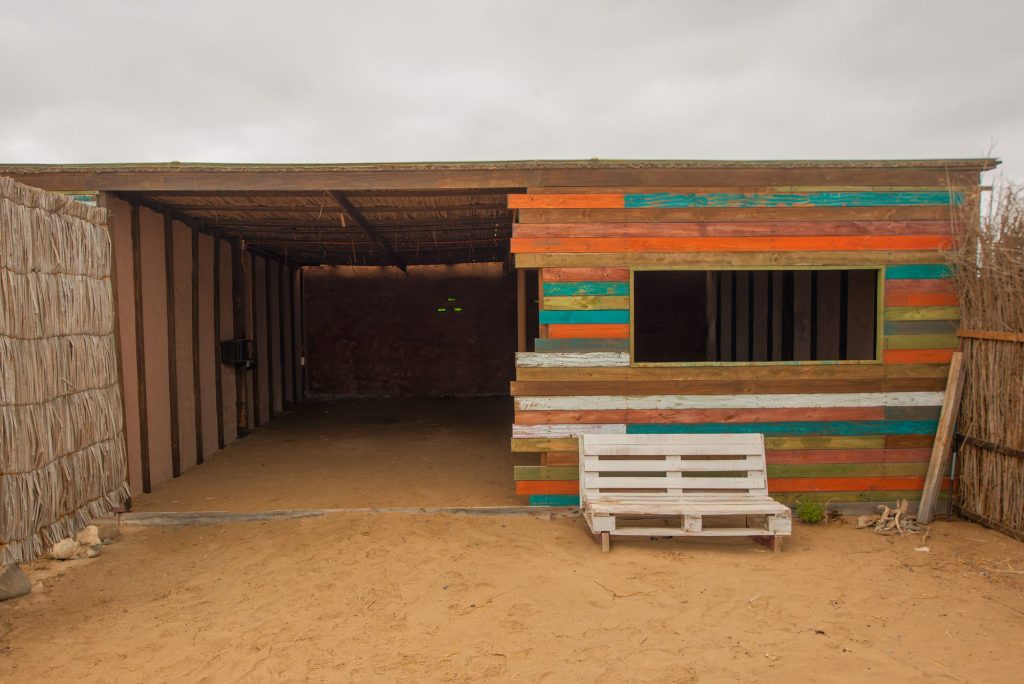 Refugio techado de madera de colores con una banca, en el camping